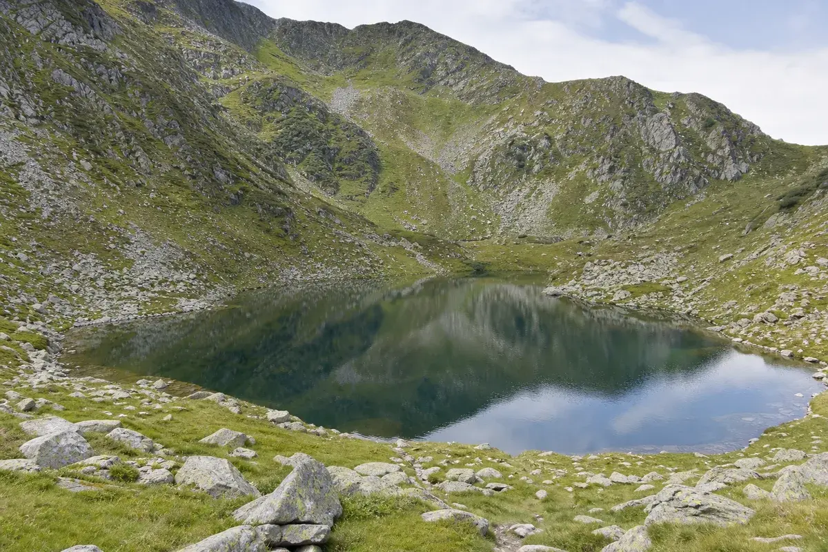 Lac glaciar mic și limpede într-o căldare alpină, cu pajiști și stânci în jur